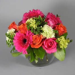 Mixed bouquet of pink gerberas, roses, and orange blooms in a glass vase