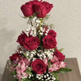 Tiered bouquet of red roses and pink flowers in a glass vase with a red ribbon