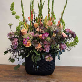 Large mixed floral arrangement in a black vase with pink and peach blooms