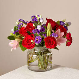 Bouquet of red roses, pink lilies, and purple flowers in a glass vase