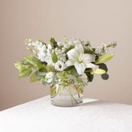White lilies and small white flowers in a clear glass vase