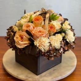 Peach and cream roses arranged in a square box with a ribbon