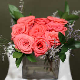 Pink roses arranged in a square glass vase with small purple filler flowers
