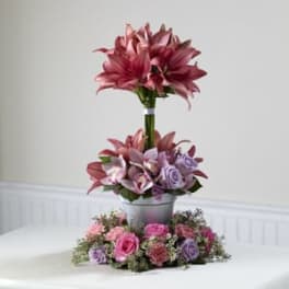 Tiered floral arrangement with pink lilies and roses in a metal container