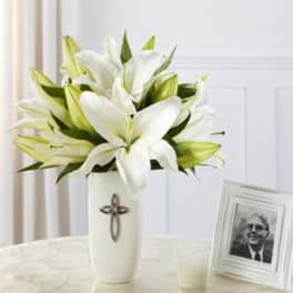 White lilies arranged in a tall vase beside a framed photo