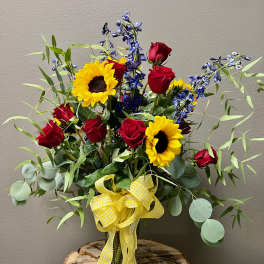 Bouquet of red roses and sunflowers in a glass vase with a yellow ribbon