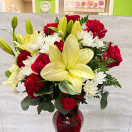 Bouquet of red roses, white chrysanthemums, and yellow lilies in a red glass vase