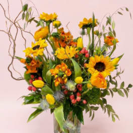 Tall yellow and orange flower arrangement with sunflowers in a clear glass vase.