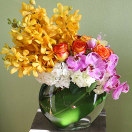 Yellow orchids, pink orchids, roses, and white hydrangeas in a glass vase
