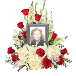 Memorial floral arrangement with red roses, white lilies, and a framed photo