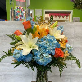Bouquet of blue hydrangeas, white lilies, and orange roses in a glass vase