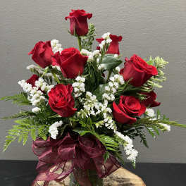 Red roses arranged in a glass vase with white filler flowers and a burgundy ribbon