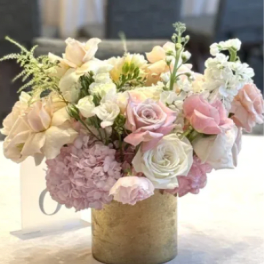 Pastel arrangement of pink hydrangeas and blush and ivory roses in a gold cylinder vase