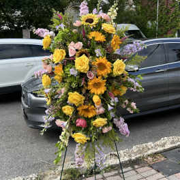 Tall standing spray of yellow roses, sunflowers, and pastel blooms