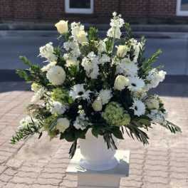 White floral arrangement in a white urn with roses and daisies
