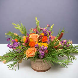 Mixed bouquet of peach, orange, yellow, and purple flowers in a patterned vase