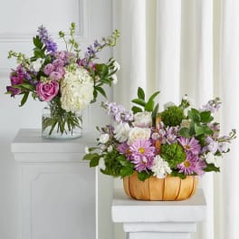 Two floral arrangements with pink, white, and purple blooms, one in a glass vase and one in a wooden basket