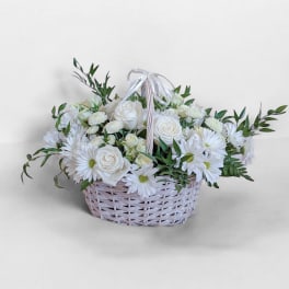 White roses and daisies in a pale woven basket with a ribbon handle
