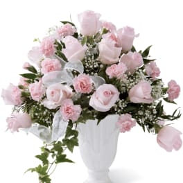 Pink roses and carnations arranged in a white vase with a sheer ribbon