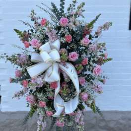 Standing floral spray with pink roses and carnations, finished with a white ribbon bow