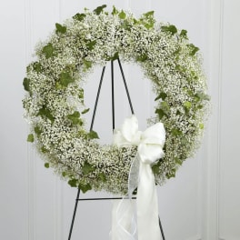 White floral wreath on a black stand with a large white ribbon bow