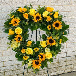Heart-shaped floral wreath with yellow roses and sunflowers on a stand