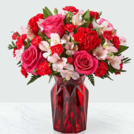 Pink roses, red carnations, and pale alstroemeria in a red glass vase