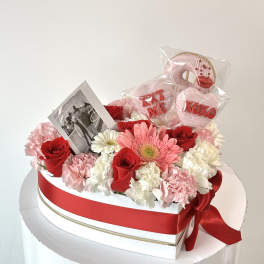 Heart-shaped flower box with red roses, pink and white carnations, and a photo card