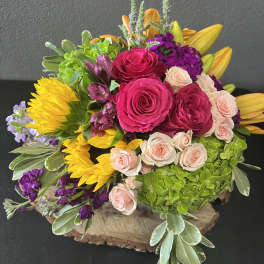 Bright mixed bouquet with roses, sunflowers, lilies, and hydrangea in a wooden base