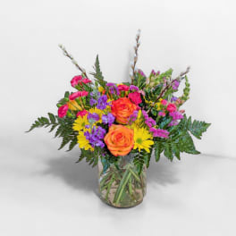 Bouquet of orange roses, yellow daisies, and purple flowers in a glass vase