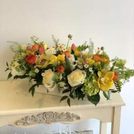 Low floral arrangement with roses, tulips, and ranunculus in a white container