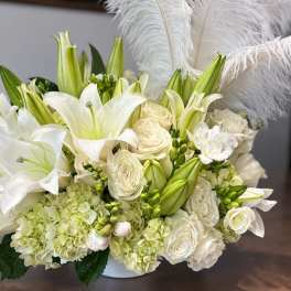 White lilies and roses arranged with feathers in a low vase