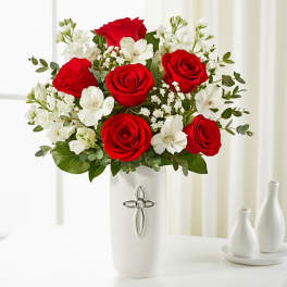 Red roses and white flowers in a white vase with a cross emblem