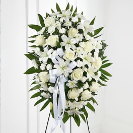 White floral standing spray with roses and lilies on a white ribboned easel