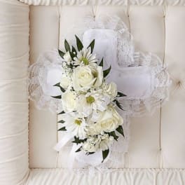 White floral cross with lace trim and ribbon on a tufted cream cushion