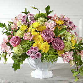Mixed pink, yellow, and green flower arrangement in a white pedestal vase