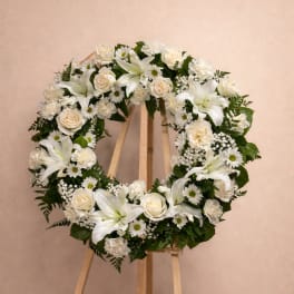 White floral wreath on a wooden easel with roses and lilies