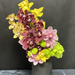Tall black vase with pink and yellow orchids and bright green blooms in a modern angled arrangement
