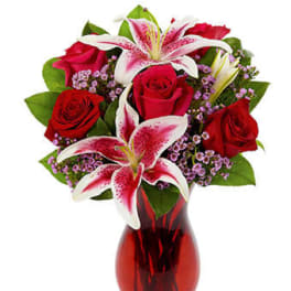 Red roses and pink lilies with purple filler flowers in a red glass vase