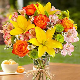 Bright bouquet of yellow lilies, orange roses, and pink alstroemeria in a clear glass vase