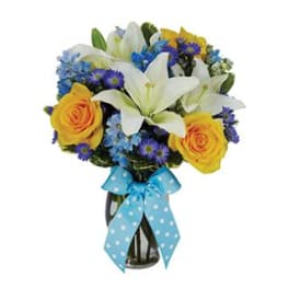 Vase arrangement of white lilies, yellow roses, and blue flowers with a blue polka dot ribbon