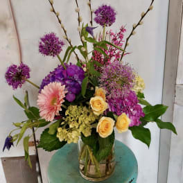 Mixed bouquet of purple, pink, and yellow flowers in a clear glass vase