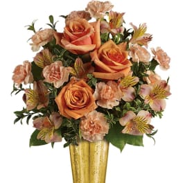 Arrangement of peach and orange roses, carnations, and alstroemeria in a tall gold vase
