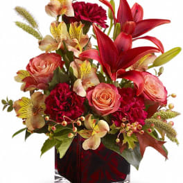 Red lilies, peach roses, and yellow alstroemeria in a square red glass vase