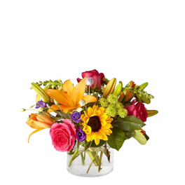 Mixed bouquet of roses, lilies, and a sunflower in a clear glass vase