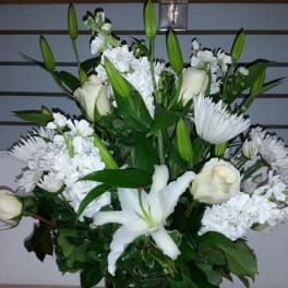 White lilies, roses, and daisies arranged in a tall glass vase