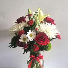 Bouquet of red roses, white lilies, and white daisies in a glass vase