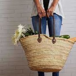 Person holding a large woven market basket with groceries and flowers