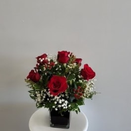 Red roses arranged in a square glass vase with white filler flowers