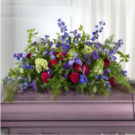 Large floral casket spray with blue, purple, pink, and white flowers